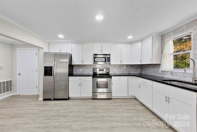 kitchen with white cabinets, sink, light hardwood / wood-style flooring, decorative backsplash, and stainless steel appliances