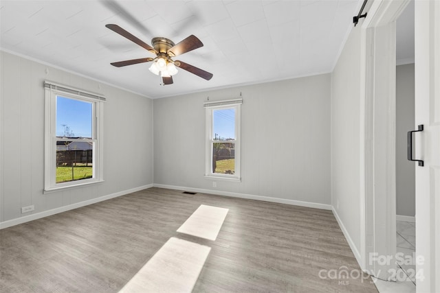 empty room with light wood-type flooring, a barn door, ceiling fan, and ornamental molding