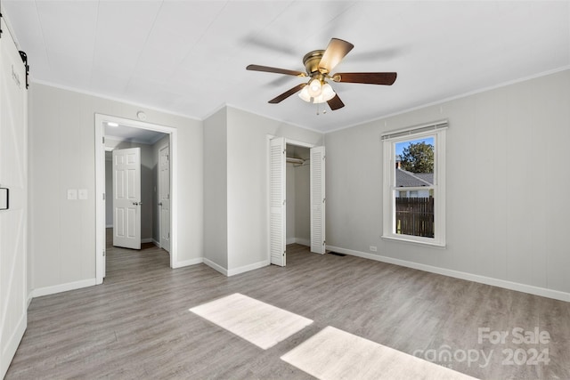 unfurnished bedroom featuring ceiling fan, crown molding, a barn door, light hardwood / wood-style flooring, and a closet