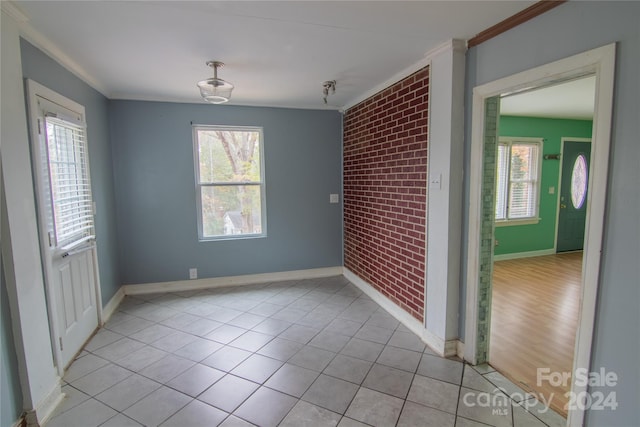 unfurnished room featuring light hardwood / wood-style floors, ornamental molding, and brick wall