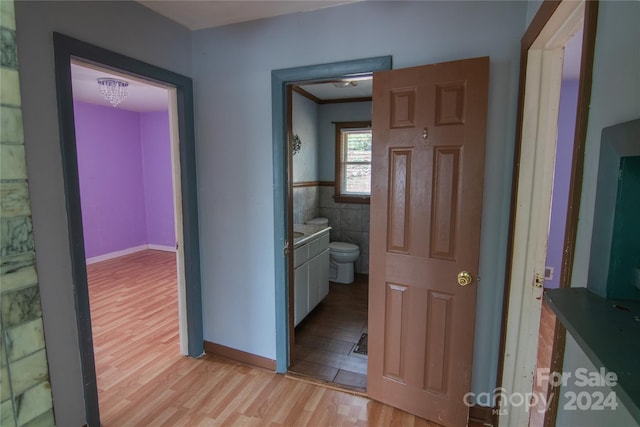 corridor featuring light wood-type flooring, tile walls, and crown molding