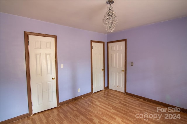 unfurnished bedroom with light wood-type flooring and a notable chandelier