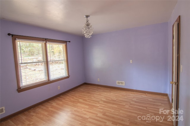 spare room featuring light wood-type flooring and an inviting chandelier