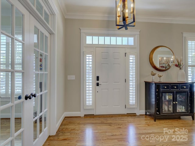 entrance foyer featuring crown molding, a notable chandelier, light hardwood / wood-style floors, and french doors