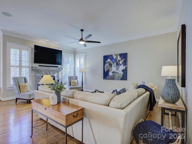 living room with light hardwood / wood-style flooring, crown molding, a stone fireplace, and ceiling fan