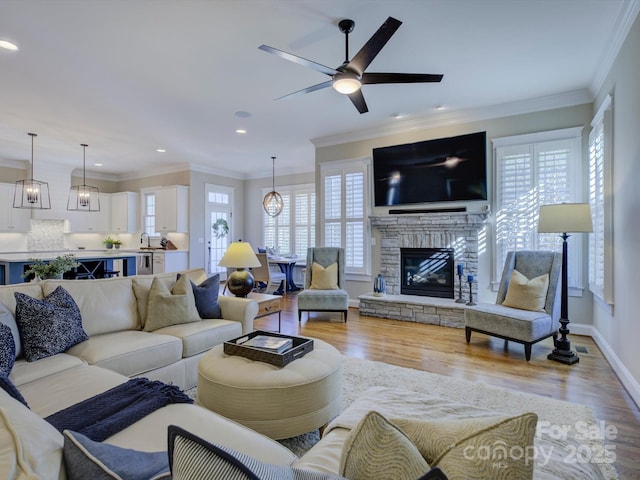 living room with crown molding, a wealth of natural light, a stone fireplace, and light wood-type flooring