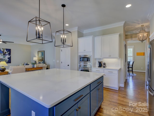 kitchen featuring appliances with stainless steel finishes, pendant lighting, white cabinets, crown molding, and blue cabinetry