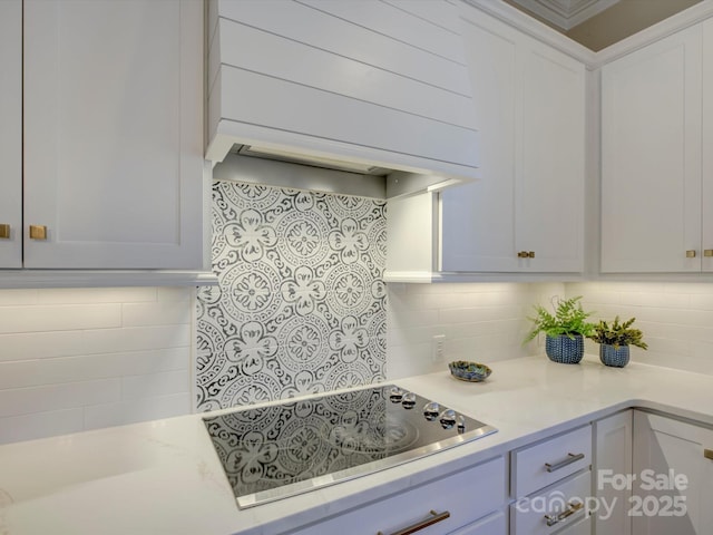 kitchen with black electric cooktop, decorative backsplash, white cabinets, and premium range hood