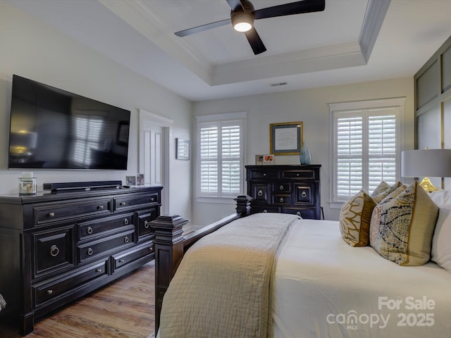 bedroom with a raised ceiling, ornamental molding, multiple windows, and light hardwood / wood-style floors