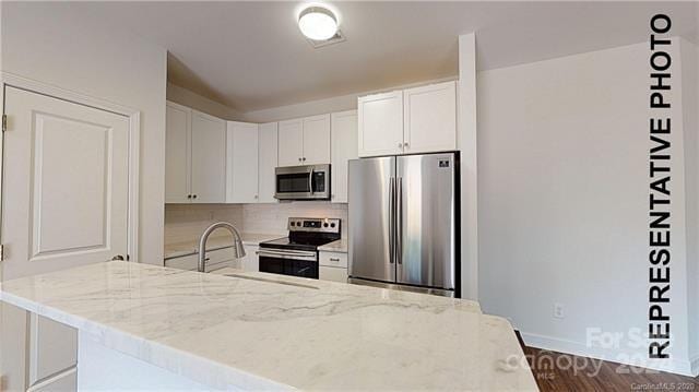 kitchen with white cabinets, appliances with stainless steel finishes, backsplash, and light stone counters