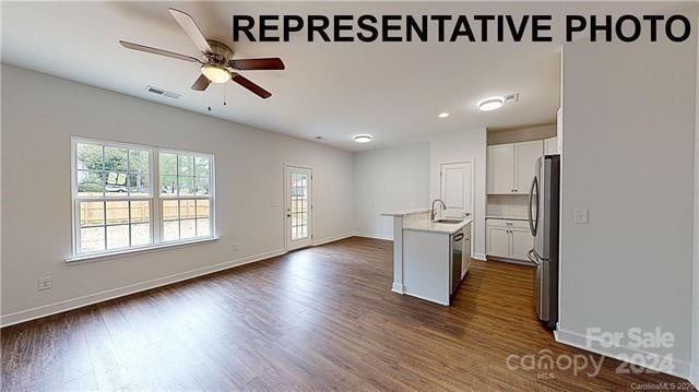 kitchen with sink, dark hardwood / wood-style flooring, stainless steel fridge, an island with sink, and white cabinets