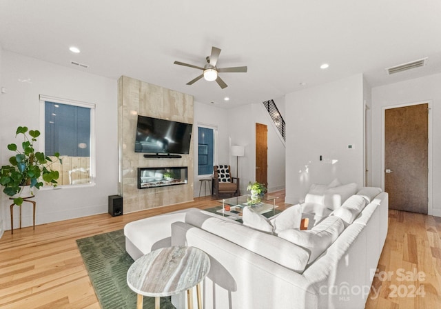 living room with ceiling fan, a fireplace, and light hardwood / wood-style floors