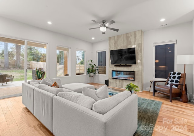 living room with ceiling fan, a tile fireplace, and light hardwood / wood-style flooring