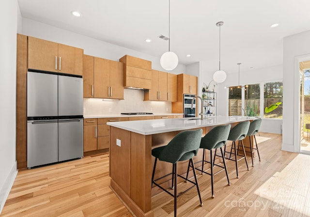 kitchen featuring a center island with sink, decorative light fixtures, light wood-type flooring, and appliances with stainless steel finishes