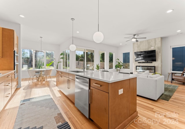 kitchen with ceiling fan, hanging light fixtures, an island with sink, appliances with stainless steel finishes, and light wood-type flooring