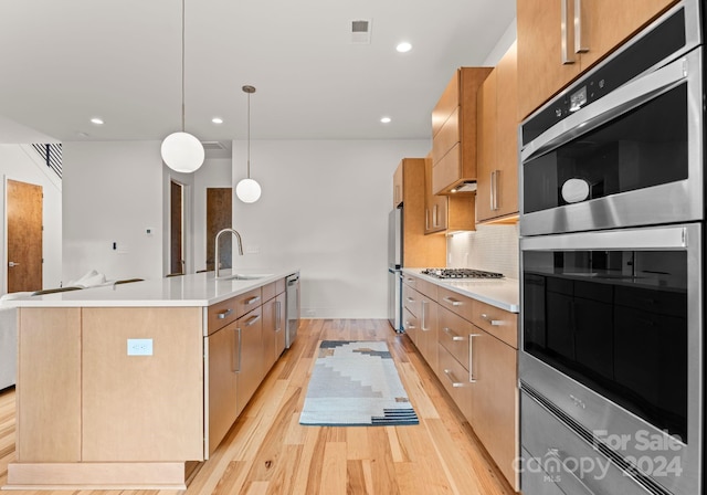 kitchen with appliances with stainless steel finishes, sink, decorative light fixtures, a center island with sink, and light hardwood / wood-style floors