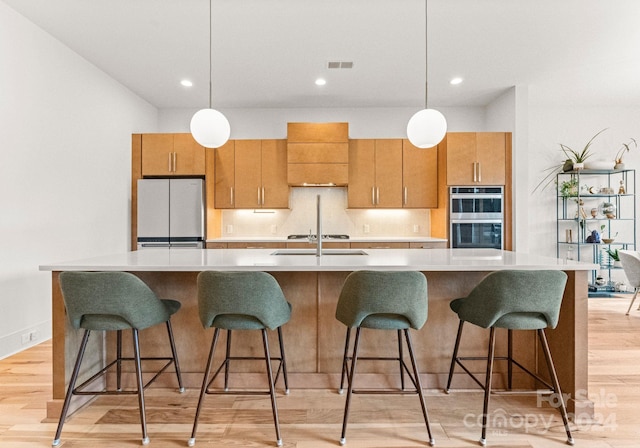 kitchen featuring double oven, an island with sink, light hardwood / wood-style floors, and white refrigerator