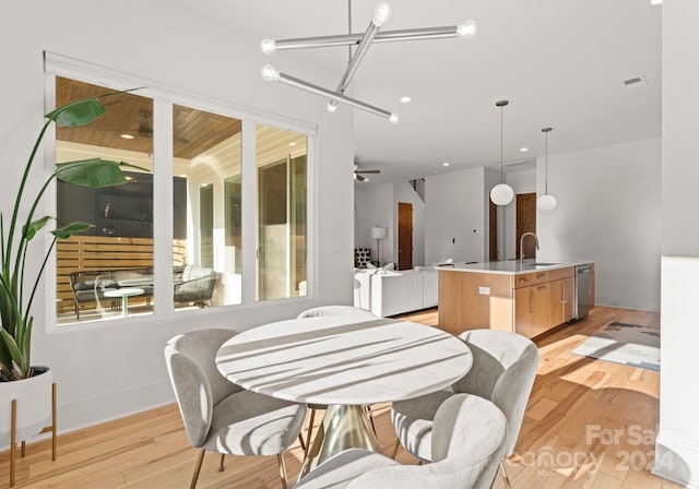 dining room featuring ceiling fan with notable chandelier, light hardwood / wood-style flooring, and sink