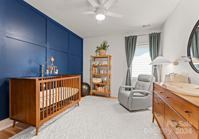 bedroom with ceiling fan, light hardwood / wood-style floors, and a crib