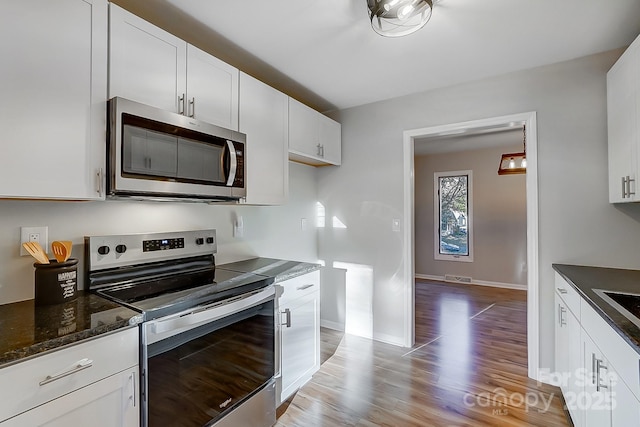 kitchen featuring light hardwood / wood-style floors, white cabinetry, stainless steel appliances, and dark stone counters