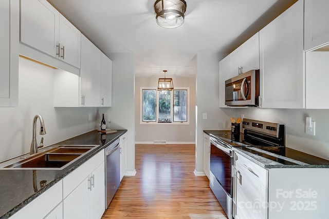 kitchen with sink, appliances with stainless steel finishes, decorative light fixtures, white cabinets, and light wood-type flooring