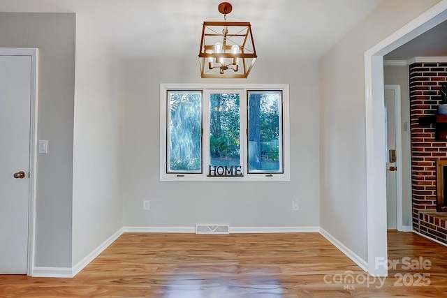 unfurnished room with a fireplace, a chandelier, and light hardwood / wood-style floors