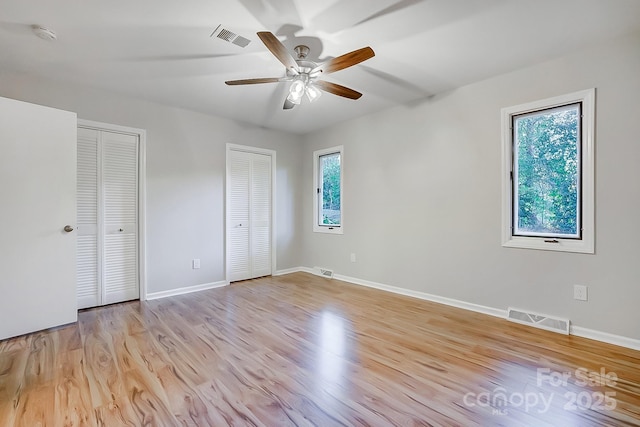 unfurnished bedroom featuring multiple windows, ceiling fan, light hardwood / wood-style floors, and two closets