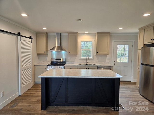 kitchen with appliances with stainless steel finishes, a barn door, wall chimney exhaust hood, and wood-type flooring