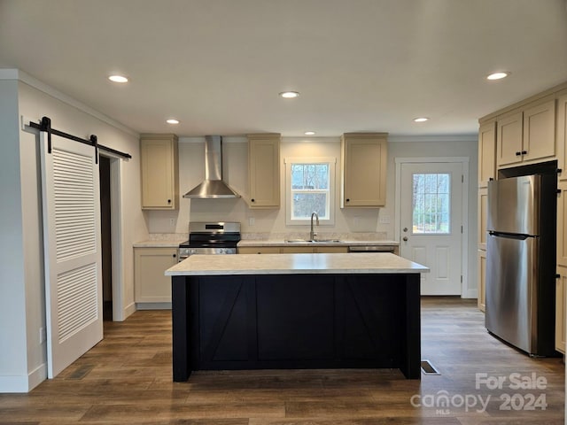 kitchen with wall chimney exhaust hood, stainless steel appliances, sink, a barn door, and hardwood / wood-style flooring