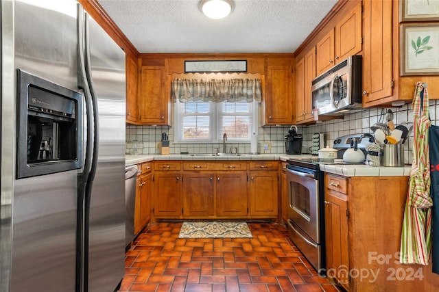 kitchen with tile countertops, sink, a textured ceiling, appliances with stainless steel finishes, and tasteful backsplash