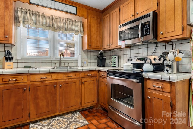 kitchen featuring decorative backsplash, stainless steel appliances, crown molding, sink, and tile counters