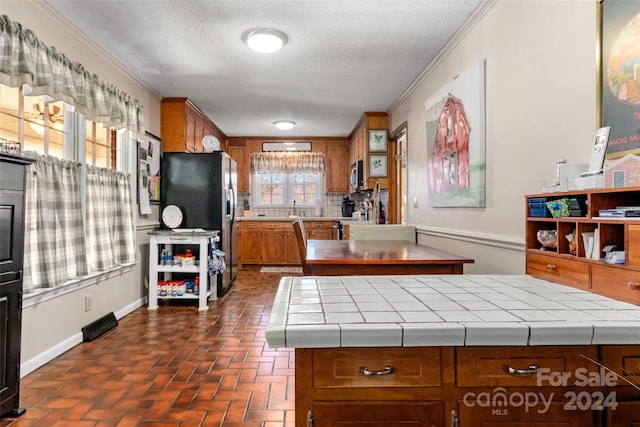 kitchen featuring sink, tasteful backsplash, tile countertops, crown molding, and stainless steel fridge