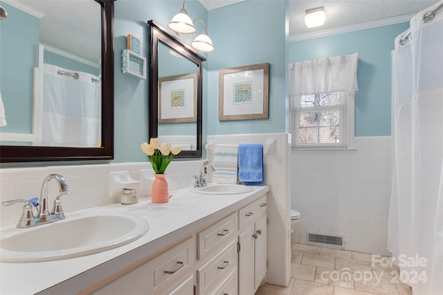 bathroom with tile patterned floors, ornamental molding, vanity, a textured ceiling, and tile walls