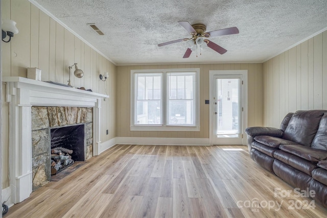 living room with a fireplace, light wood-type flooring, crown molding, and wooden walls