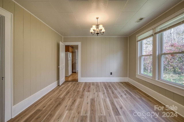 spare room with wood walls, light hardwood / wood-style floors, and an inviting chandelier