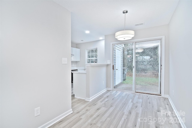 unfurnished dining area with a textured ceiling and light wood-type flooring