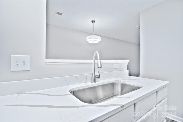 kitchen featuring white cabinetry, light stone countertops, sink, pendant lighting, and a textured ceiling