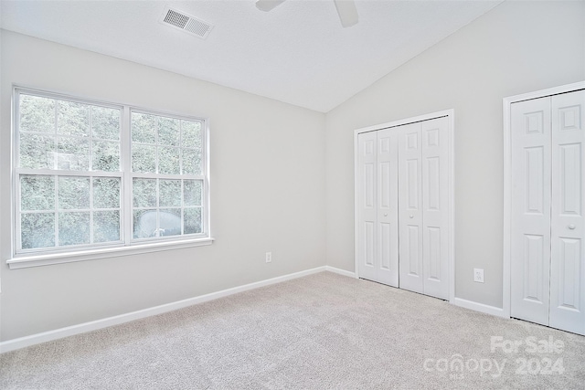 unfurnished bedroom with carpet floors, two closets, ceiling fan, and lofted ceiling