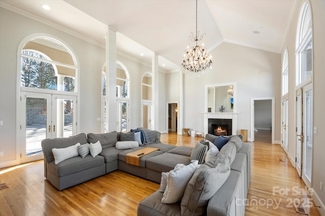 living room featuring light hardwood / wood-style flooring, an inviting chandelier, high vaulted ceiling, ornamental molding, and french doors