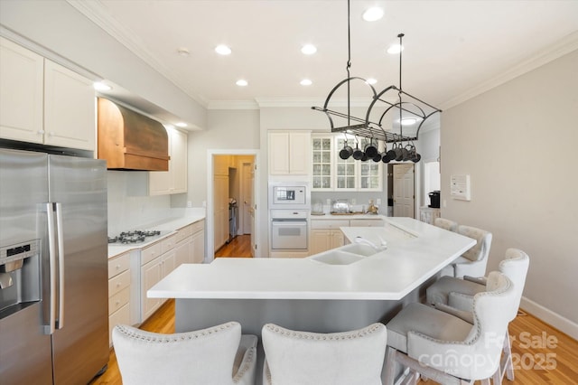 kitchen featuring sink, white cabinets, custom exhaust hood, a kitchen island with sink, and white appliances