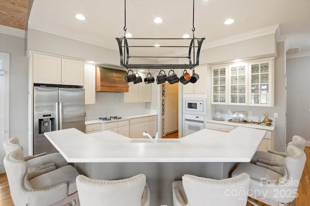 kitchen with white appliances, a breakfast bar, custom range hood, and a large island with sink