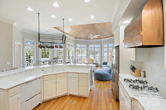 kitchen featuring sink, decorative light fixtures, ornamental molding, stainless steel fridge, and wall chimney range hood