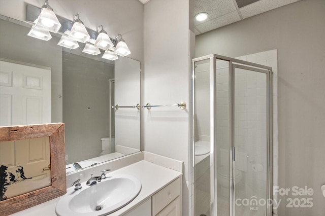 bathroom featuring vanity, a shower with shower door, toilet, and a drop ceiling