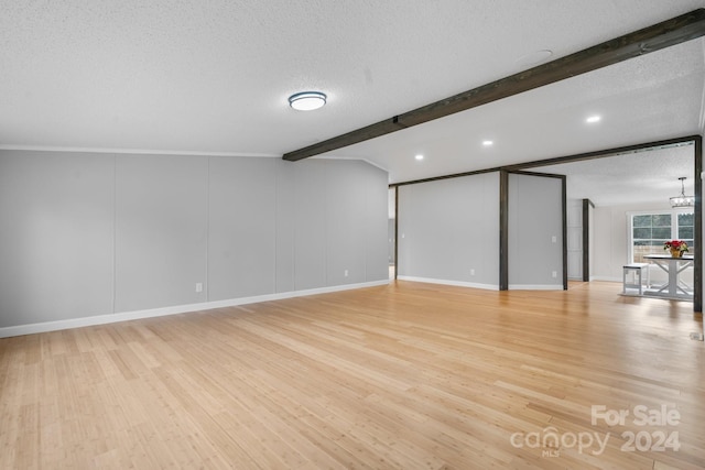 empty room with a notable chandelier, beamed ceiling, a textured ceiling, and light wood-type flooring