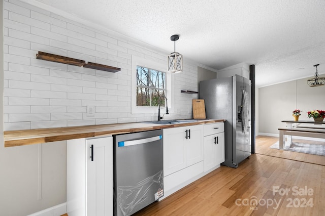 kitchen with wooden counters, white cabinets, hanging light fixtures, light wood-type flooring, and appliances with stainless steel finishes