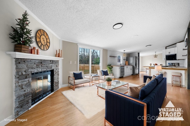 living room featuring a textured ceiling, a fireplace, light wood-type flooring, and crown molding