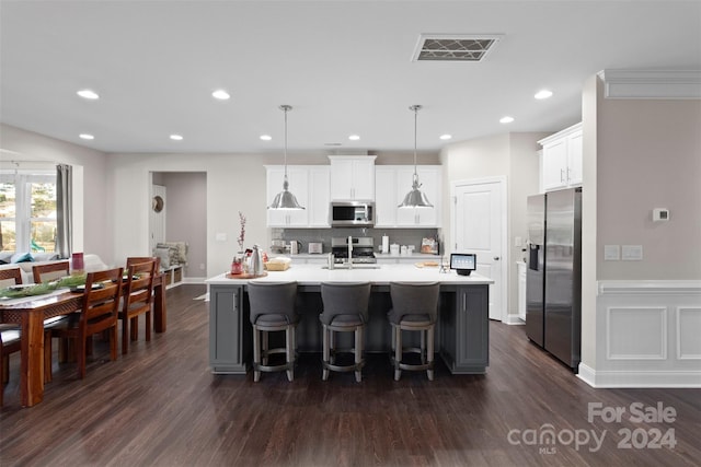 kitchen with pendant lighting, dark wood-type flooring, stainless steel appliances, and an island with sink