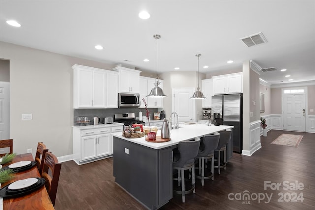 kitchen with white cabinets, an island with sink, hanging light fixtures, and appliances with stainless steel finishes