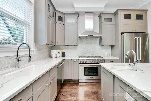 kitchen featuring high quality appliances, sink, wall chimney exhaust hood, light stone countertops, and dark hardwood / wood-style flooring