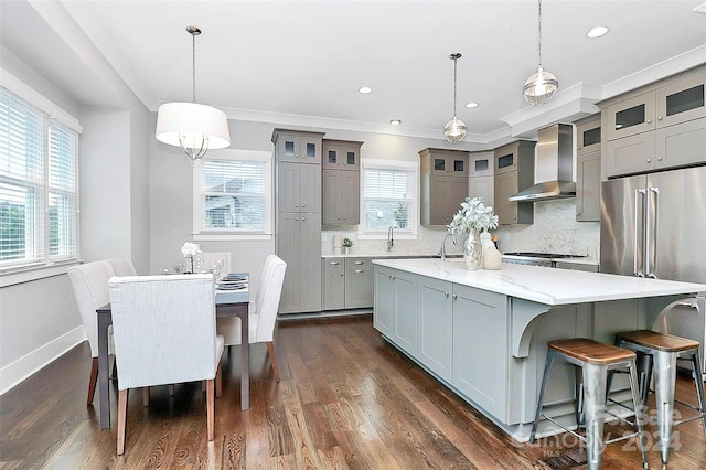 kitchen with tasteful backsplash, wall chimney exhaust hood, dark wood-type flooring, a spacious island, and hanging light fixtures